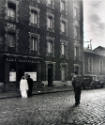 A black and white photograph of a man walking in the middle of a street toward newlyweds in fro…