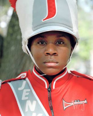 A close-up of a young girl wearing a red and white marching band hat and jacket.