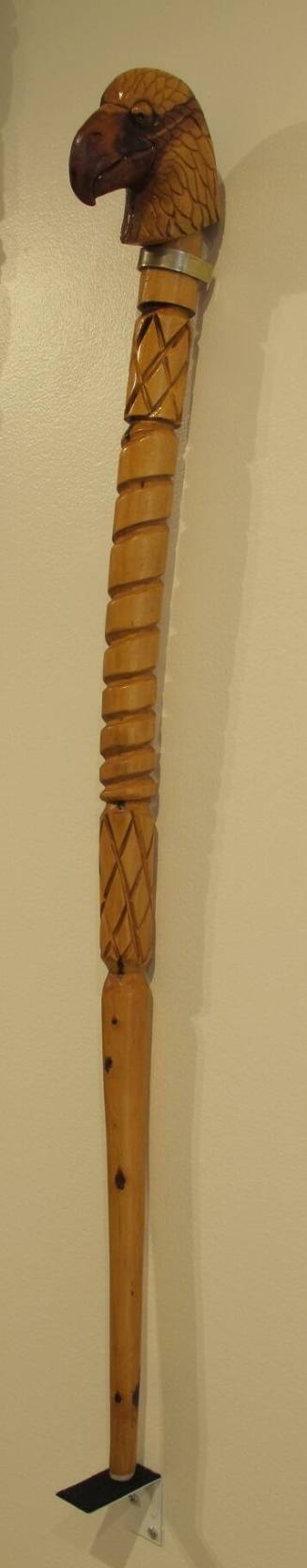 A carved walking stick with an eagle's head and alternating patterns of diamonds and spirals. 