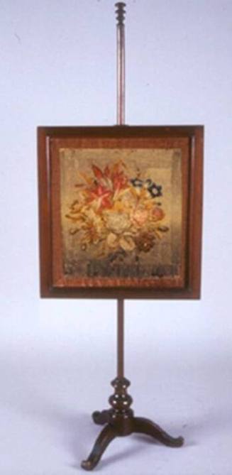 An adjustable fire screen with framed needlework stitched with a bouquet of multi-colored flowe…