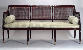 A Sheraton-style scroll-back cane settee with a carved crest rail, shaped and reeded arms suppo…