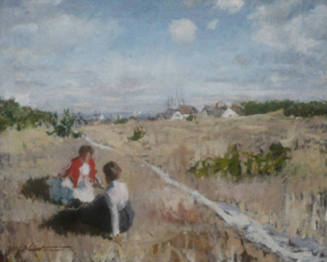 Two conversing women are seated by a path leading through the grassy dunes to a seaside town. 