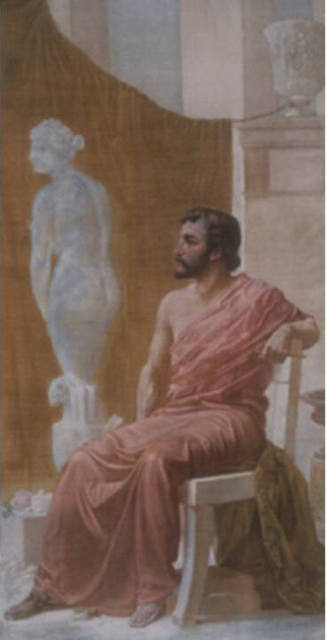A man in a red robe holds a chisel and a hammer and sits next to a sculpture of a Greek goddess…