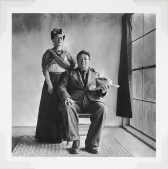 A black and white photographic portrait in an interior setting showing Diego Rivera seated hold…