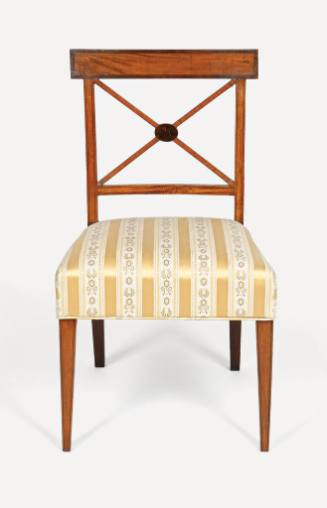 A side chair with a X-shaped cross bar and an upholstered seat in green with gold stripes. 
