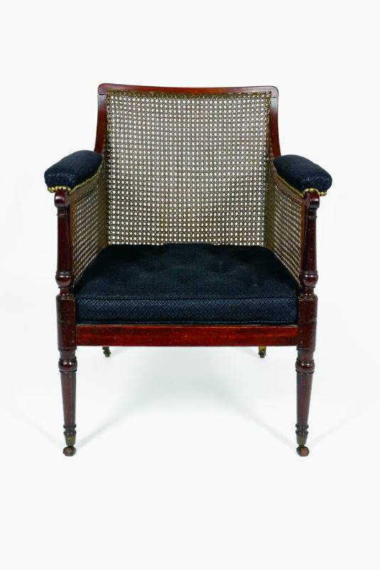 A mahogany armchair with caned back, sides, and seat supported by turned legs on casters. The a…