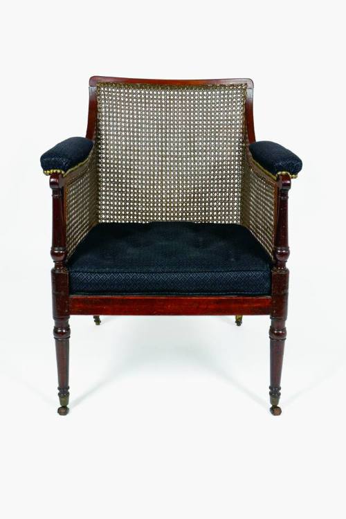 A mahogany armchair with caned back, sides, and seat supported by turned legs on casters. The a…
