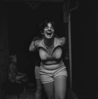 A black and white photograph of a teenage girl wearing a halter top and shorts, laughing, with …