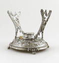 A silver stand embellished with a repousse alpine scene and pierced arms surmounted by rams' he…