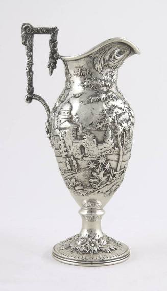 A silver cream pitcher embellished with a repousse alpine scene on an urn-shaped body mounted a…