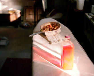 Sunlight streaming through a bottle of embalming fluid next to a bowl of cherries on an ironing…