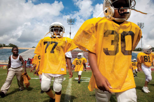 A group of young boys in football jerseys and white helmets walking across a football field.