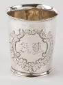 A silver beaker with a scalloped and c-scroll engraved medallion.