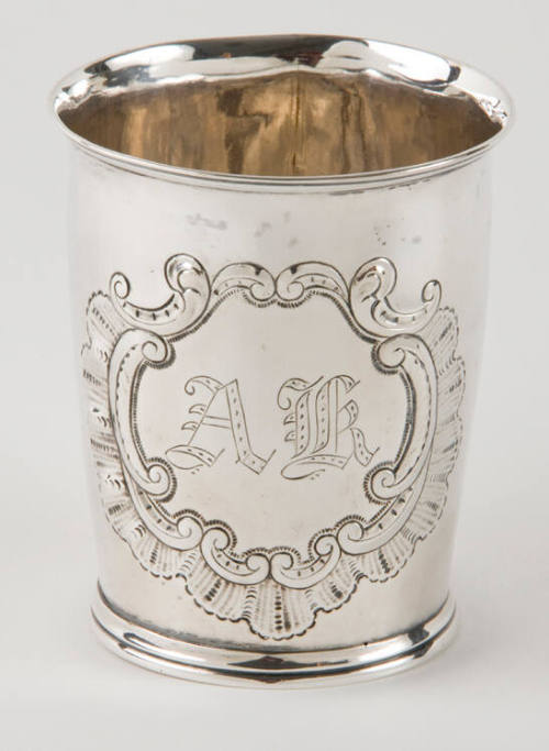 A silver beaker with a scalloped and c-scroll engraved medallion.