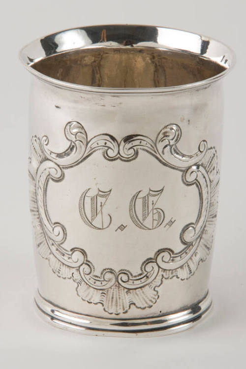 A silver beaker with a scalloped and c-scroll engraved medallion.