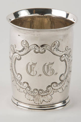 A silver beaker with a scalloped and c-scroll engraved medallion.