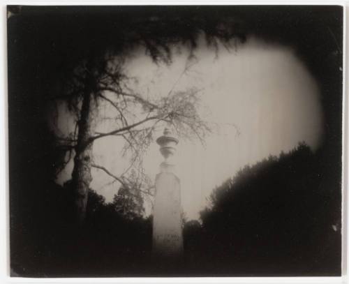 An urn-topped obelisk centered in the photograph is surrounded by dark shadows.