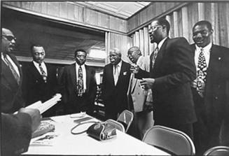 A black and white photograph of a group of men standing around a table signing.