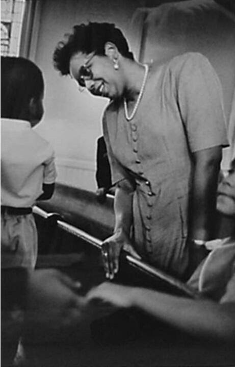 A black and white photograph of the back of a little boy standing on a church pew talking to a …