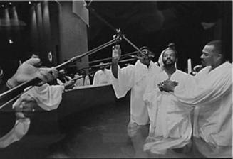 A black and white photograph of a man being baptized with microphones hovering over the baptism…