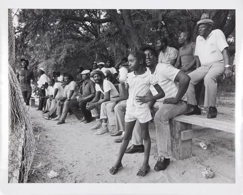 A black and white photograph of individuals watching a sporting event with a young girl in the …