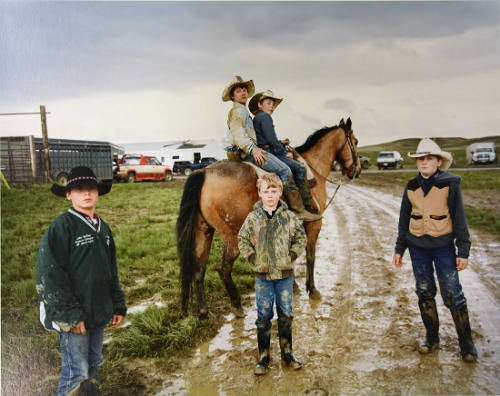 A color photograph of a group of three boys standing and two seated on a horse on a muddy dirt …