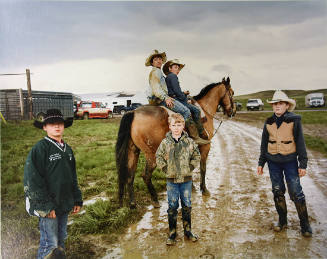 A color photograph of a group of three boys standing and two seated on a horse on a muddy dirt …