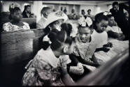 A black and white photograph of a row of girls talking in a church pew.