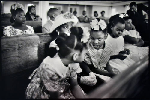 A black and white photograph of a row of girls talking in a church pew.