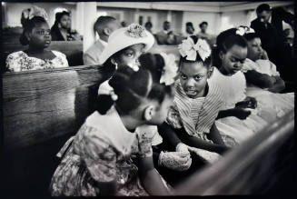 A black and white photograph of a row of girls talking in a church pew.
