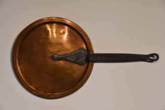 A circular copper plate with an iron handle.