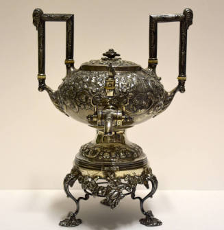 A melon-shaped urn with two high rectangular handles resting atop a stand with a burner. 