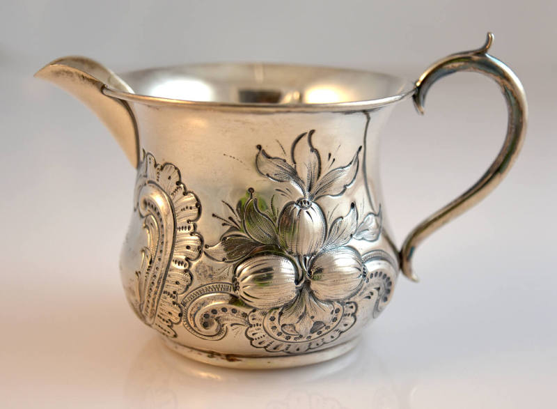 A cream pitcher with an S-shaped handle with foliate repoussé decoration by an eagle.  