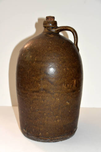 A brown-glazed ceramic jug with a drip design allover, a short neck and a handle extending from…