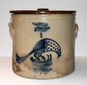A cream-colored crock with a flat brown lid topped with a flat knob. The crock is painted with …