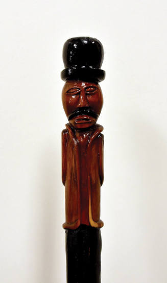 A mustached man with a top hat carved on the upper third of the walking stick.