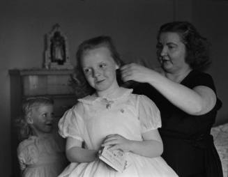 A black and white photograph of a girl having her hair braided.
