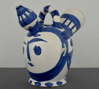 Blue and white vessel with a face painted on the side under one of two spouts with a handle on …
