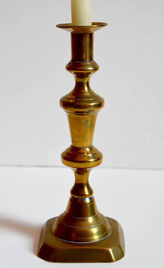 One of a pair of brass candlesticks with a square base and cut corners.