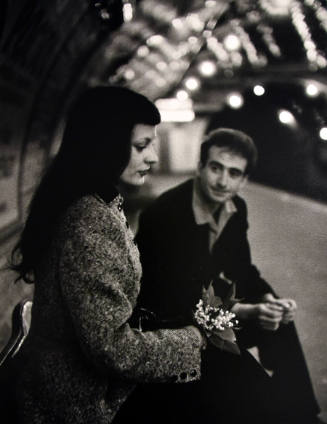A black and white photograph of a man and a woman sitting in a subway station.