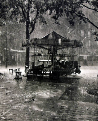 A black and white photograph of a small carousel in the rain.