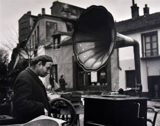 A black and white photograph of a man looking at a Victrola.