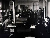 A black and white photograph of several men standing around a pool table.