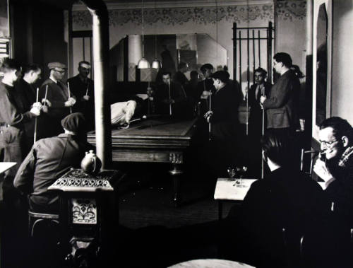 A black and white photograph of several men standing around a pool table.