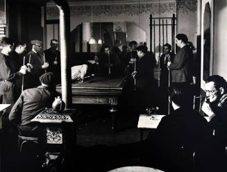 A black and white photograph of several men standing around a pool table.