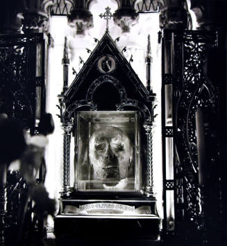 A black and white photograph of the head of a man in a decorative reliquary. 
