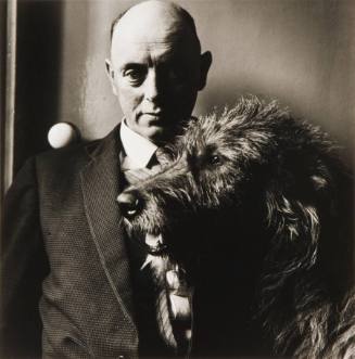 A black and white photograph of a man in a suit with a shaggy Irish Wolfhound dog. 