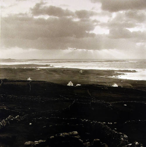 A black and white photograph of the countryside in a patchwork of low stone walls, where just b…