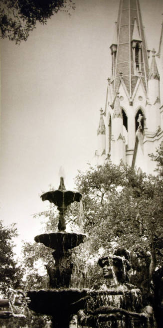 A woman standing by a fountain with a church spire in the background on the right. 