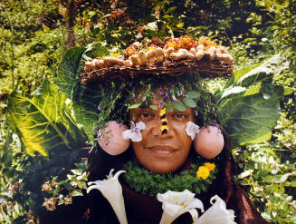 A woman wears peaches as earrings and a hat made from leaves, flowers and peanuts.